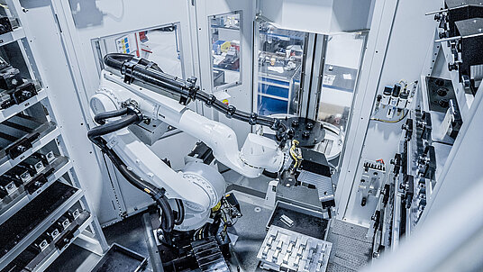 Der HERMLE Roboter bedient beide HERMLE-Bearbeitungszentren mit Bauteilen rund um die Uhr. Drei Regalspeichermodule mit Matrizen- und Palettenplätzen sowie Spannmittel- und Greiferplätzen sorgen für eine optimale Teilebereitstellung. 